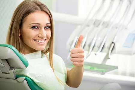 Smiling woman in dental chair giving a thumbs up